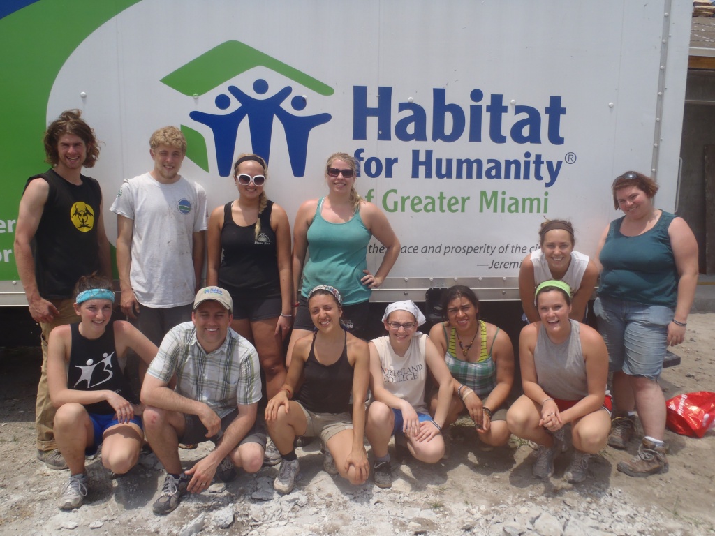 12 college students grouped for a photo with the Habitat for Humanity of Greater Miami van on a construction site during spring break